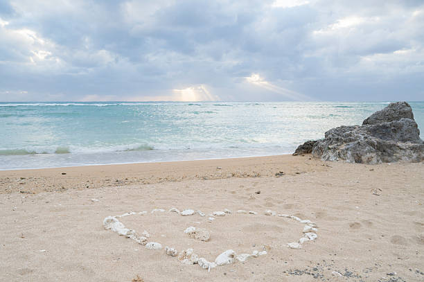 Heart shape on the sand of a beach with cloudy sky background.