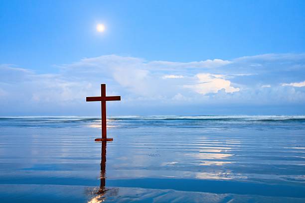 Wood cross on a New Zealand beach with storm clouds on the horizon. Also the moon is still showing through the clouds on a dawn sky.