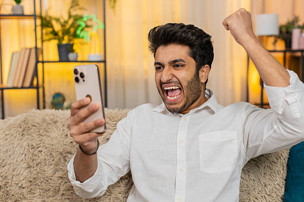 istock Indian joyful man on sofa happily texting on smartphone, celebrating lottery win, joyful expression 2227041670