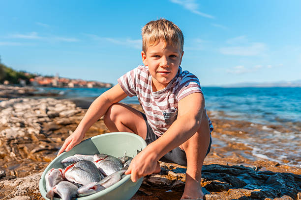 Young boy holding up a crappie fish he just caught while fishing from a dock on a summer evening.