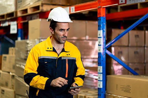 istock Caucasian male warehouse supervisor holding digital tablet analyzing logistics status while walking beside stacked cardboard boxes in industrial storage facility during stock management 2227046033