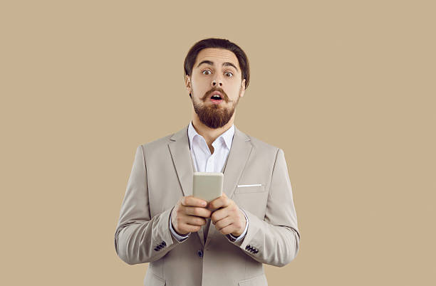istock Stylish emotional man holding mobile phone and looking at camera with shocked expression. 2227050267