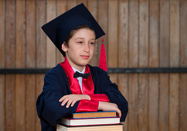 Primary school graduation portrait. Boy graduating, leaning on his books in front of a wooden wall.