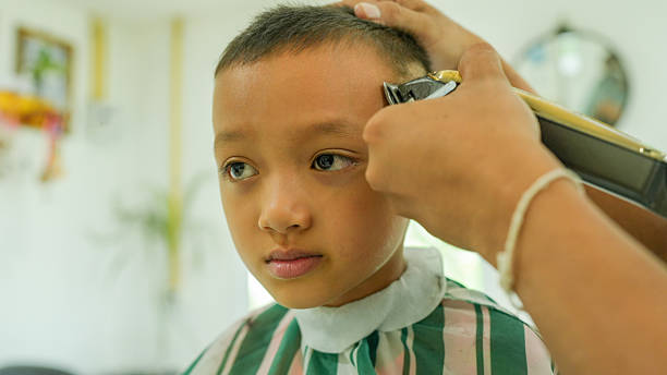 Child getting haircut in barbershop, showing focused expression while barber uses clippers. atmosphere is calm and professional, highlighting grooming process