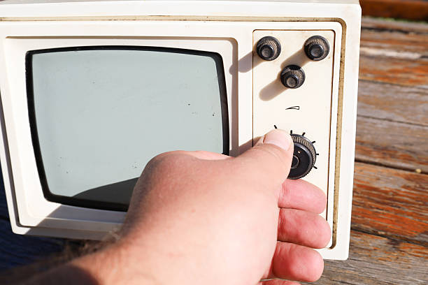 A human hand adjusts settings on an old portable television resting on a wooden surface. This shot emphasizes interaction with vintage technology, evoking nostalgia for past eras.