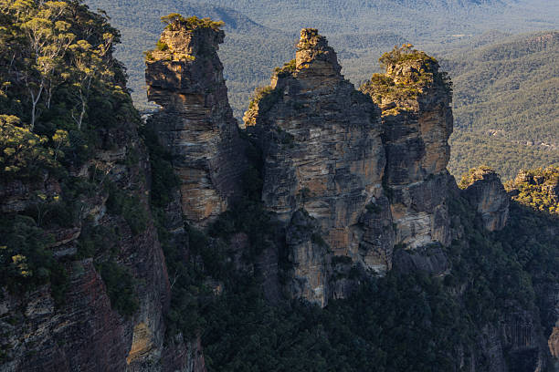 The Three Sisters, a rock formation in the Blue Mountains of New South Wales, Australia, stand tall against a backdrop of lush greenery, showcasing the natural beauty and geological wonders of the region.