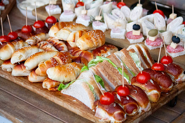 Stacked arrangement of mini sandwiches filled with cream cheese and walnuts, served on a plate garnished with fresh cherry tomatoes.