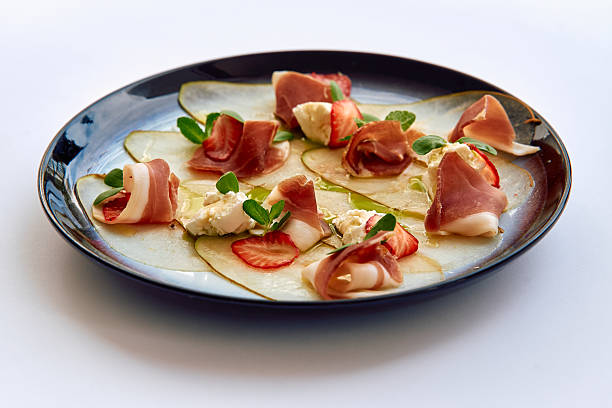 istock A Culinary Delight Featuring Delicate Prosciutto and Sweet Strawberries on a Bed of Thinly Sliced Pears, Artfully Presented on a Glazed Plate 2227087205