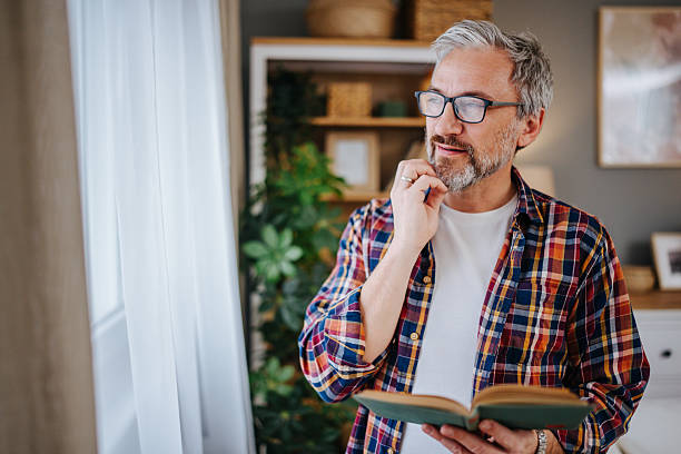 istock Pensive mature man reading a book and looking out the window 2227088278