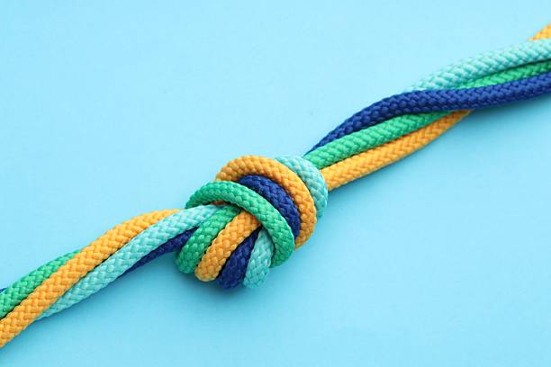 Colorful ropes tied in knot on light blue background, closeup. Unity concept