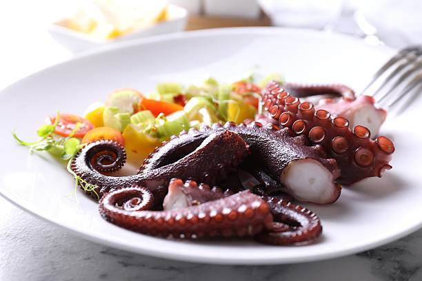 istock Plate with tasty boiled octopus tentacles and salad on white table, closeup 2227093979