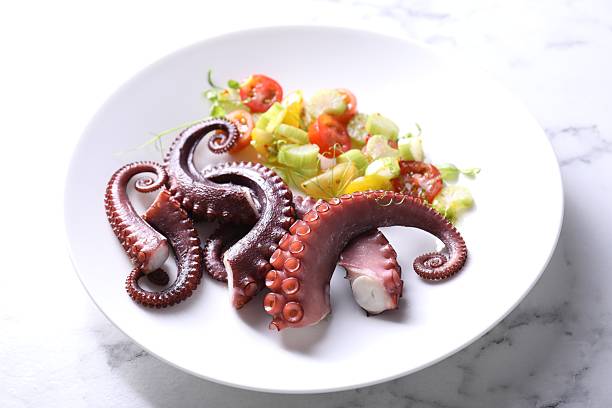 istock Plate with tasty boiled octopus tentacles and salad on white marble table, closeup 2227094022