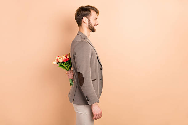 istock Photo of charming handsome gentleman dressed blazer holding back tulips looking empty space isolated beige color background 2227094571