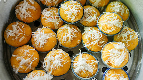 Steamed cupcakes with vibrant orange color, topped with shredded coconut, are arranged neatly steaming tray. These delightful treats are perfect for dessert lovers, showcasing blend of flavors
