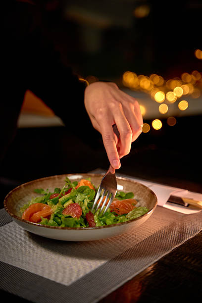 istock A Close-Up of a Hand Elegantly Using a Fork to Enjoy a Fresh and Vibrant Salad in a Dimly Lit Atmosphere with Warm Bokeh Lights in the Background 2227098058