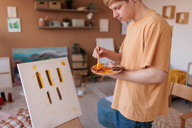 Dedicated young male artist creates a new piece while painting in his living room, using the space as a personal studio full of color and imagination.