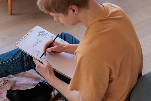 Young male artist sits on the floor of his messy living room, absorbed in drawing sketches with pencil, surrounded by scattered supplies and inspiration.