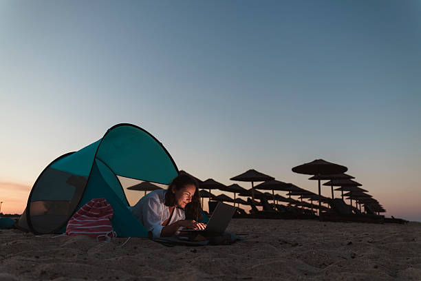 istock Woman using laptop computer on the beach at dusk 2227106820