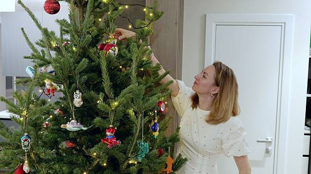 istock Woman hanging colorful ornaments, stringing twinkling lights on christmas tree, creating warm holiday ambiance in cozy home interior 2227114985