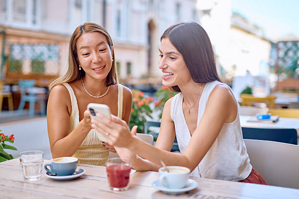 istock Two young women using smartphone and smiling at outdoor cafe 2227118322