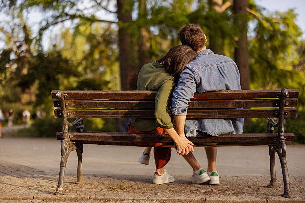 Beautiful couple bonding and smiling while sitting outdoors on a bench, enjoying warm weather and quality time.