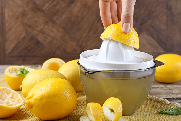 Woman with lemon using juicer at wooden table, closeup