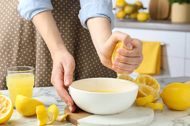 istock Woman squeezing lemon juice into bowl at marble table, closeup 2227122807