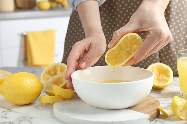 istock Woman squeezing lemon juice into bowl at marble table, closeup 2227122808