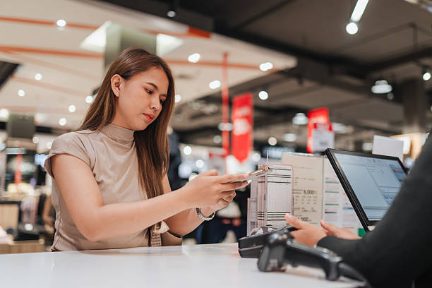 istock Asian woman making a digital payment using smartphone at retail checkout counter. Depicts modern cashless transactions, shopping convenience, and smart lifestyle in a commercial setting. 2227123365