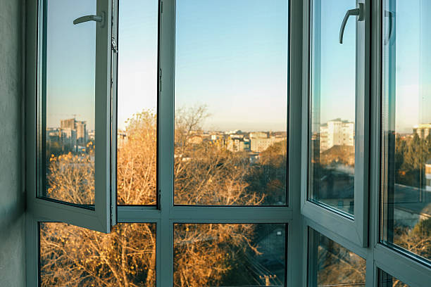 istock Panoramic city view through large glass windows with autumn trees and open vent, basked in warm sunset light 2227126363