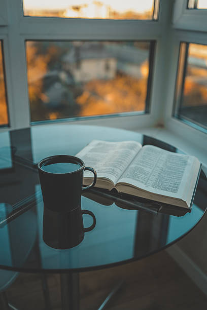 istock Open book and black coffee cup on glass table by the window, with warm sunset light reflecting through the glass and soft autumn background 2227126366