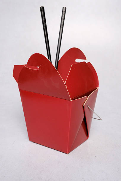 Red Chinese food box with black chopsticks isolated on gray background.