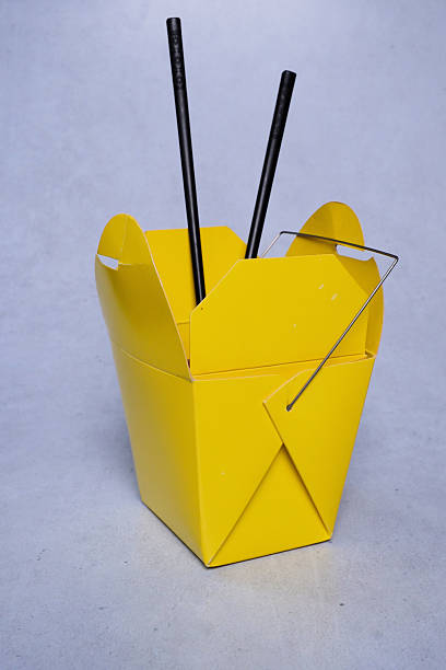Yellow chinese food box with black chopsticks and isolated on gray background.
