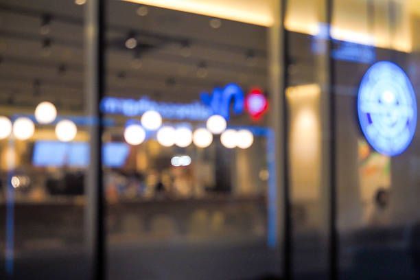 A blurred background of a modern shopping mall features sleek architecture, bright ambient lighting, and a bustling atmosphere. The scene captures wide walkways, stylish storefronts, and shoppers moving about, all softly out of focus to highlight the lively and contemporary environment. This depiction conveys a vibrant and fashionable shopping experience in a chic urban setting.