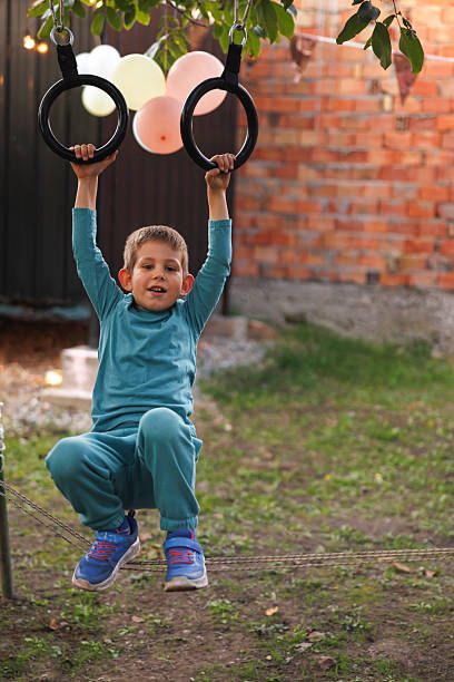 Close-up of children's hands gripping gymnastic rings outdoors with clear blue sky, concept of sport, strength and play