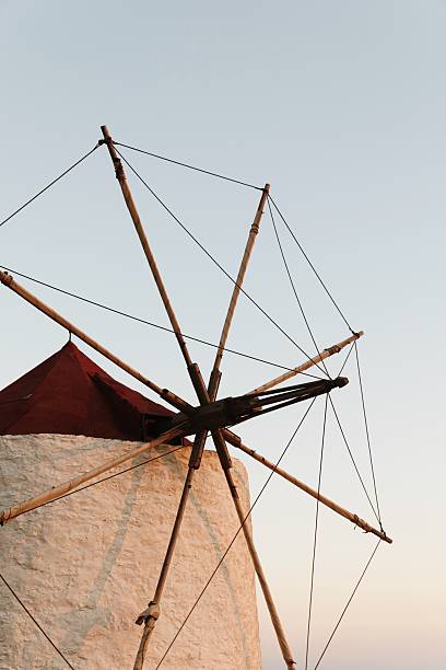 A close-up of a traditional Cycladic windmill on the Greek island of Amorgos, beautifully lit by the warm light of sunset. The red conical roof and wooden sails stand out against the pastel sky, capturing the charm of Greek island heritage.