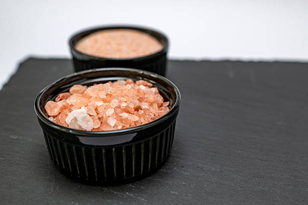 Two black cups with himalayan salt, small and medium size, placed on a black stone surface, areal view, studio shot, conceptual.