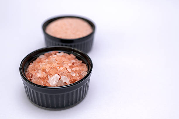 Two black cups with himalayan salt, small and medium size, placed on a white background surface, areal view, studio shot, conceptual.