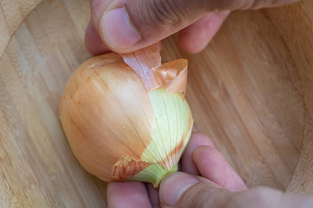 istock Hands Peeling Fresh Onion Skin on Wooden Board 2227149704