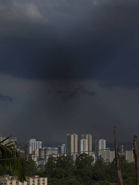 buildings on the horizon, illuminated by sunlight, with storm clouds in the background - MOGI DAS CRUZES,  SAO PAULO,  BRAZIL.