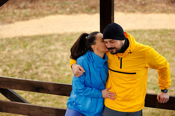 A young adult biracial couple kiss affectionately while enjoying a beautiful day outside, on a pedestrian park bridge.