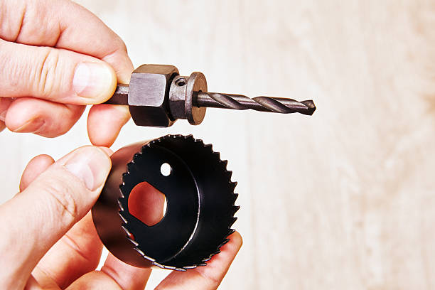 Mandrel with pilot drill bit held in one hand hole saw with teeth held in other hand unassembled woodcutting tool components visible from side angle.