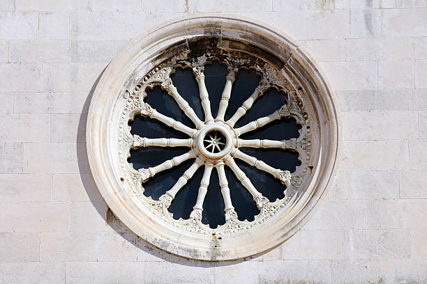 A circular carved stone rose window adorned with ornate tracery decorates a pale stone church facade, highlighting skilled Gothic craftsmanship and religious architectural heritage