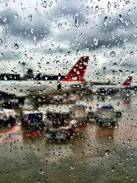 View from inside an aircraft during heavy rain, looking out at another plane and airport activity through a water-speckled window.