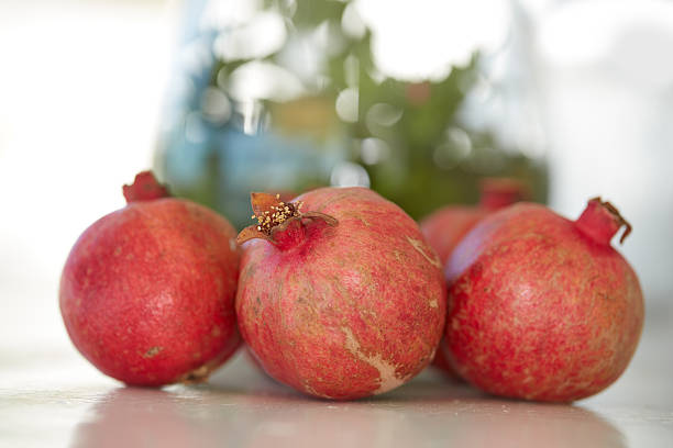 Focused composition featuring three red pomegranate fruits, with Latin name Punica granatum, placed on a bright surface, expressing fresh natural ripeness and healthy living inspiration.