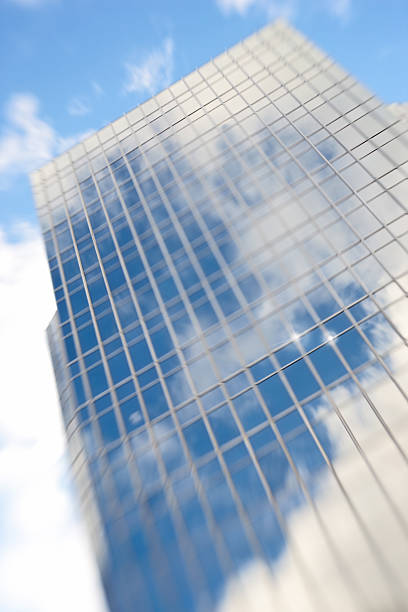 A stunning visual showcasing the contemporary design of a high-rise building. Its mirrored glass facade captures the natural beauty of clouds and the bright blue sky, creating a surreal urban landscape.