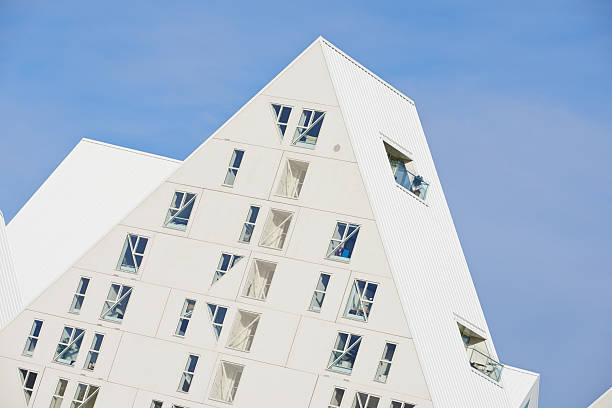Geometric modernist apartment complex features striking angled rooftops and triangular windows. The clean white surface elegantly contrasts with the vibrant blue sky, reflecting innovative design and urban aesthetics.