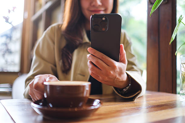 istock Closeup image of a woman holding and using mobile phone while drinking coffee in cafe 2227179199
