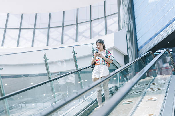 istock Young woman standing on escalator using mobile phone in modern building 2227181445