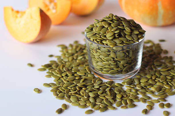 istock Glass jar filled with green pumpkin seeds or pepitas on a white surface, surrounded by scattered seeds 2227184568